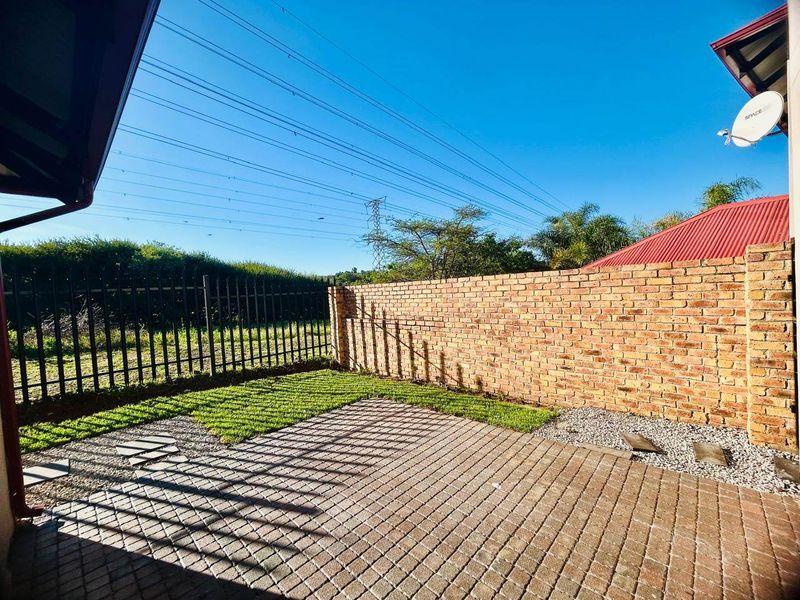 A private rear courtyard featuring a paved patio area, a brick boundary wall, and a metal security fence.