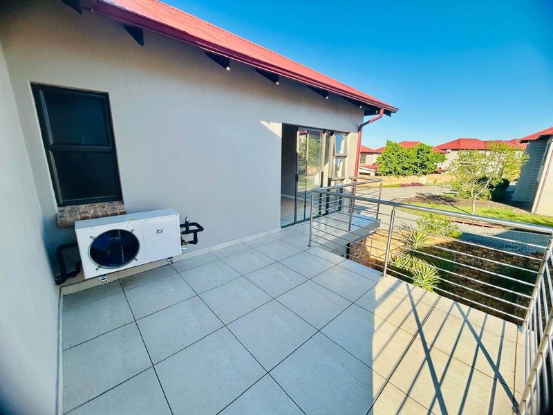 A spacious upper-level balcony featuring modern tiled flooring, a stainless steel balustrade, and a heat pump unit, offering views of the surrounding estate.