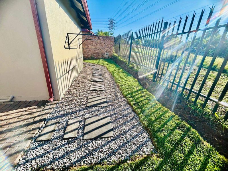 A well-maintained side garden area featuring gravel landscaping, paver stepping stones, a manicured lawn, and secure metal perimeter fencing.
