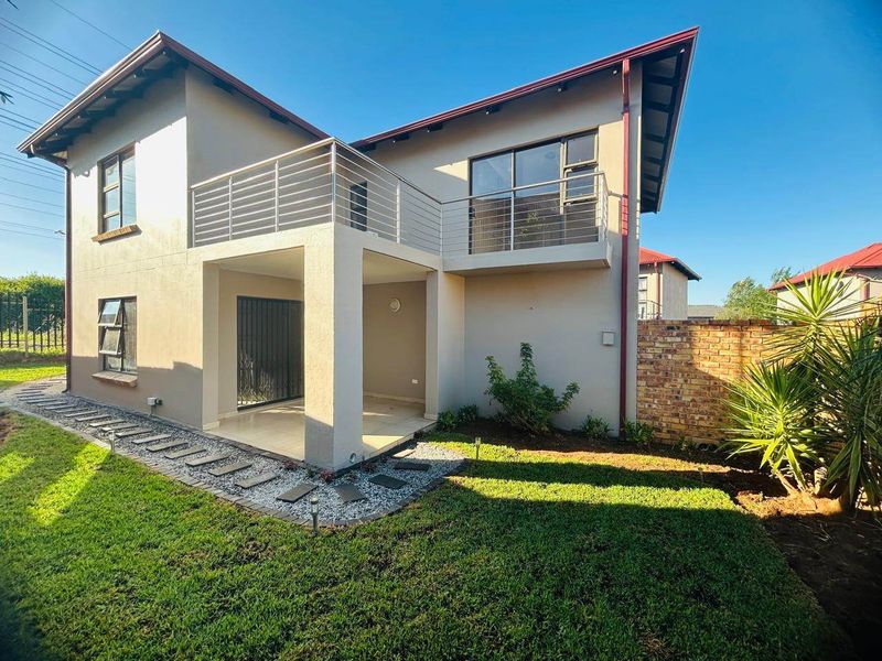 Rear view of the townhouse featuring a covered patio, an upper-level balcony with stainless steel balustrades, and a landscaped garden with a paved walkway.