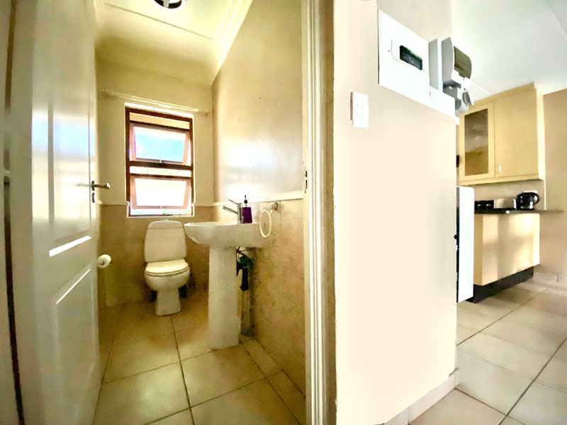 A compact guest bathroom featuring a pedestal basin and toilet, with tiled flooring and adjacent access to the kitchen area.