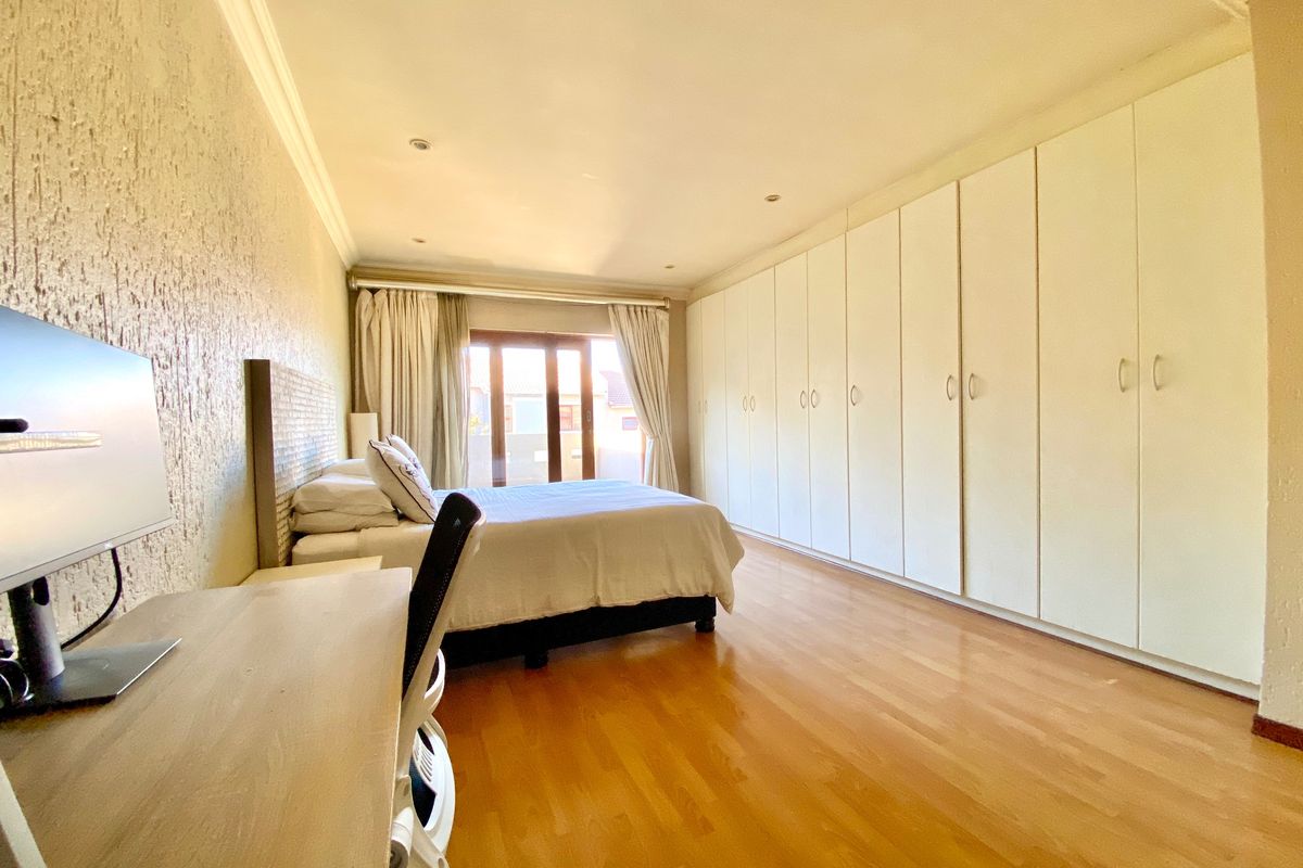 Spacious bedroom featuring extensive built-in cupboards, warm laminated flooring, and a sliding door providing natural light and access to the exterior.