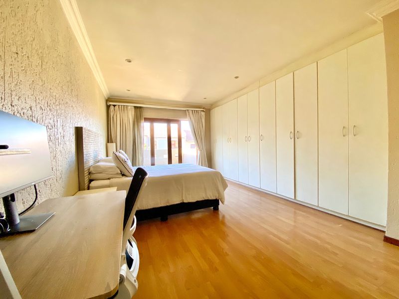 Spacious bedroom featuring extensive built-in cupboards, warm laminated flooring, and a sliding door providing natural light and access to the exterior.