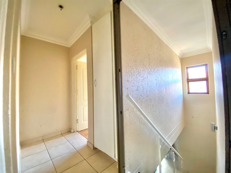 A vacant upper-level hallway featuring tiled flooring, a built-in cupboard, and a staircase with a metal railing, showing signs of wear on the walls.