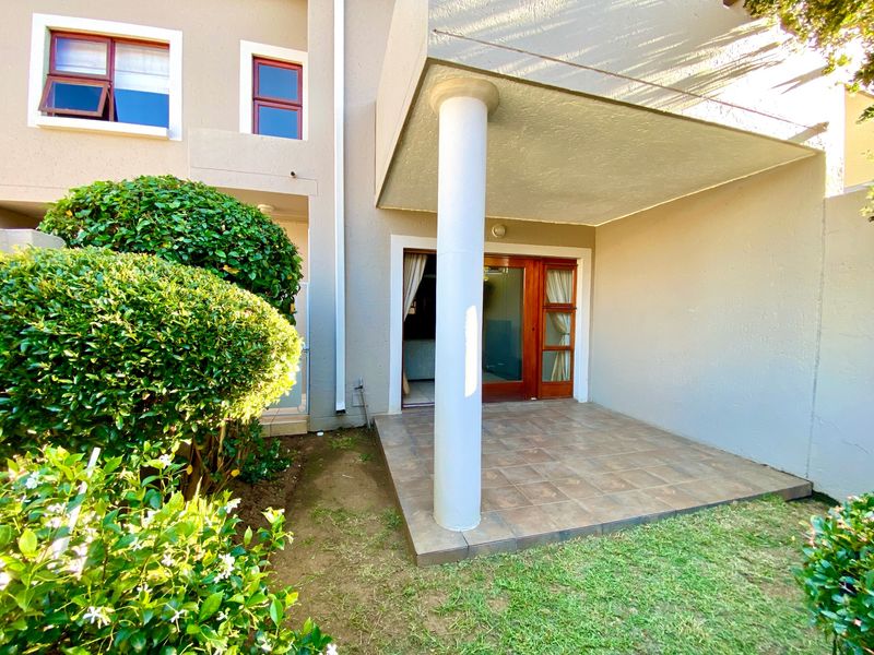 A covered patio area featuring tiled flooring and a support column, providing direct access to the interior through wooden framed glass sliding doors.