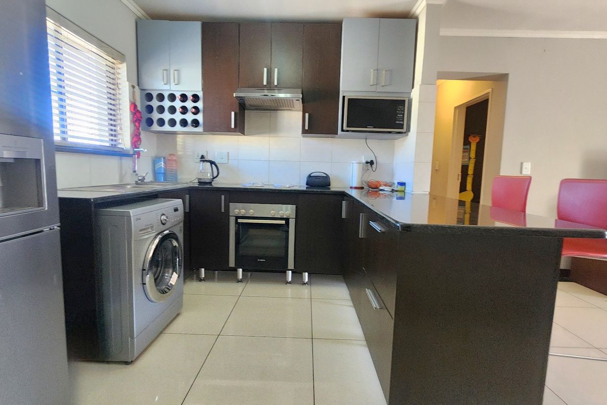 Modern kitchen featuring dark cabinetry, granite countertops, built-in oven, extractor fan, and a breakfast bar, with tiled flooring throughout.