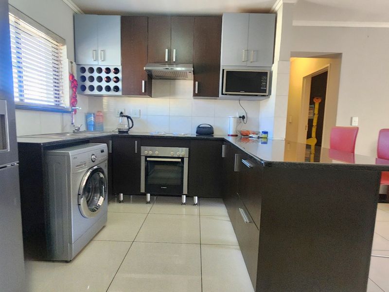 Modern kitchen featuring dark cabinetry, granite countertops, built-in oven, extractor fan, and a breakfast bar, with tiled flooring throughout.