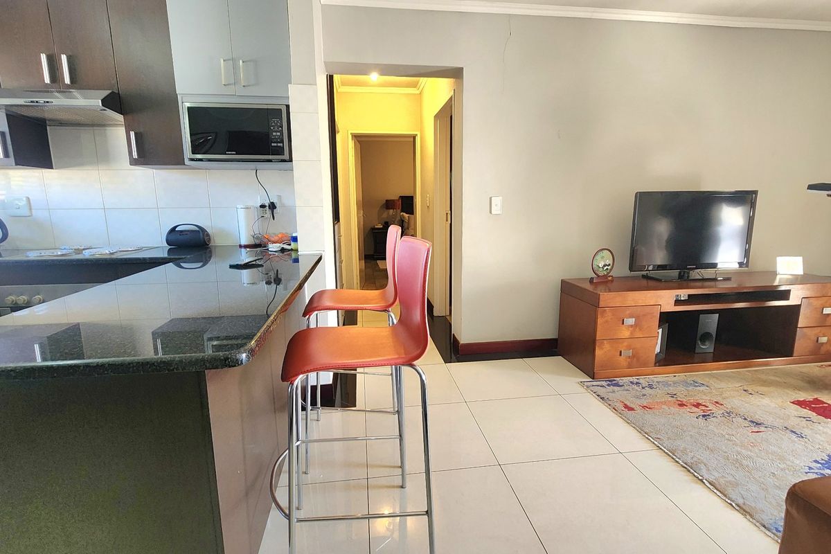 Open-plan living area featuring a kitchen with granite countertops, breakfast bar, and tiled flooring, leading into a hallway.