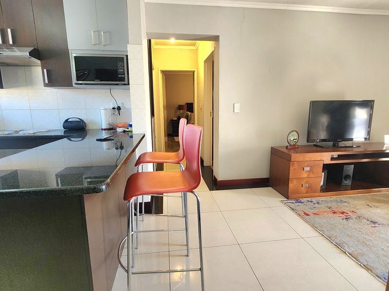 Open-plan living area featuring a kitchen with granite countertops, breakfast bar, and tiled flooring, leading into a hallway.