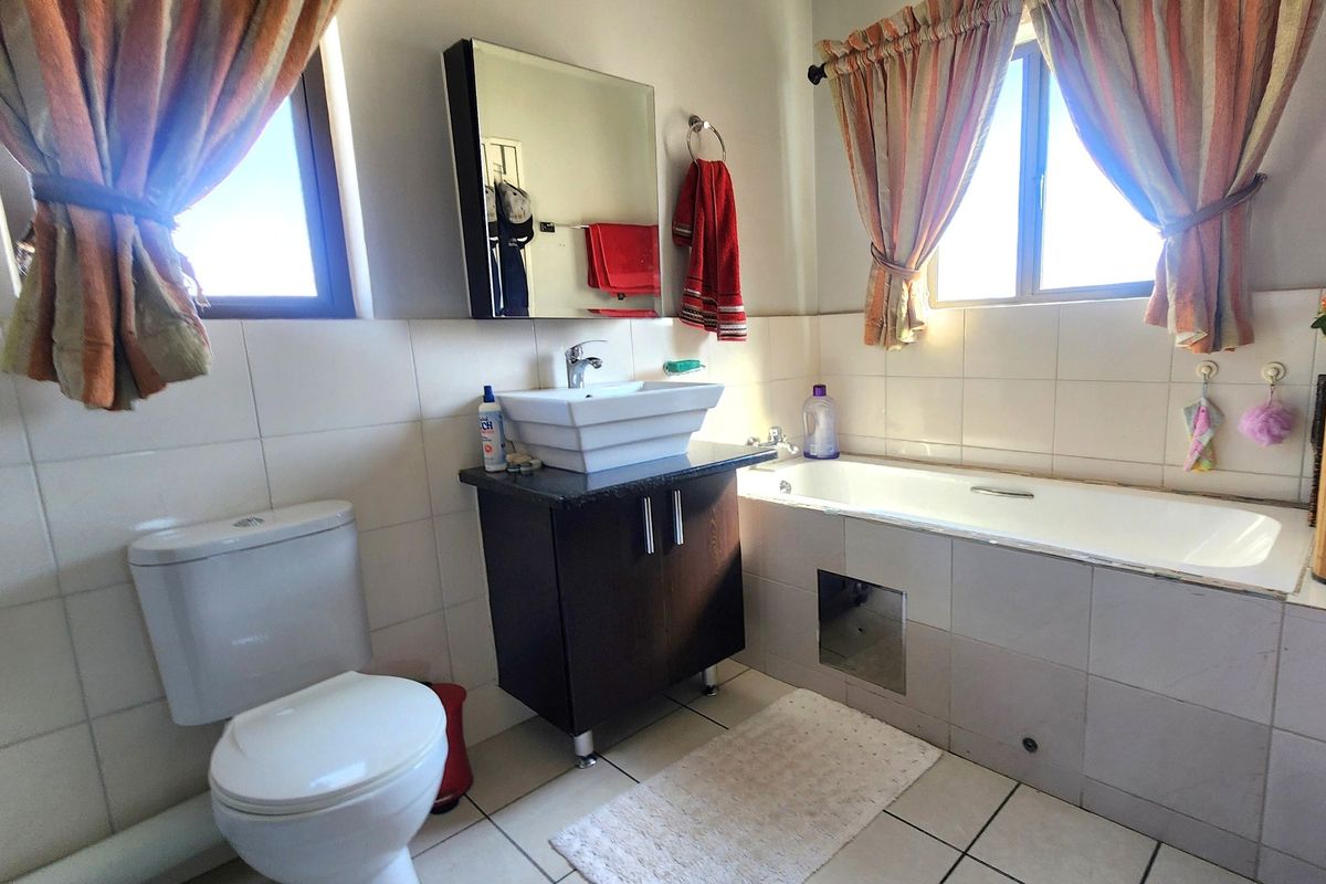 A functional bathroom featuring a vessel sink vanity, bathtub, and toilet with tiled finishes throughout.