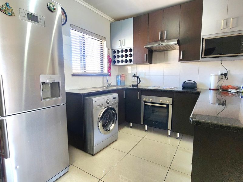 Modern kitchen featuring dark wood cabinetry, granite countertops, built-in oven, extractor fan, and integrated microwave, complemented by tiled flooring and natural light.
