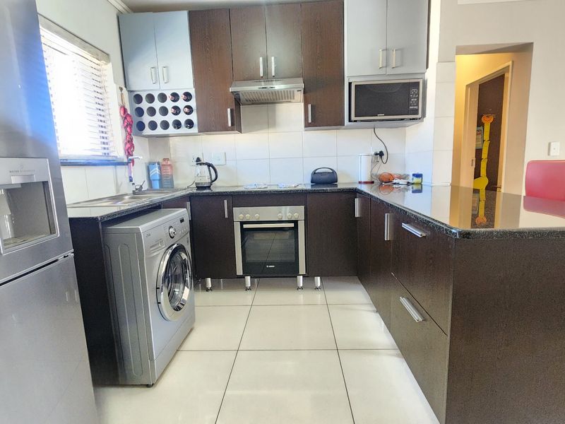 Modern kitchen featuring dark wood cabinetry, granite countertops, built-in oven, extractor fan, and integrated microwave with tiled flooring.