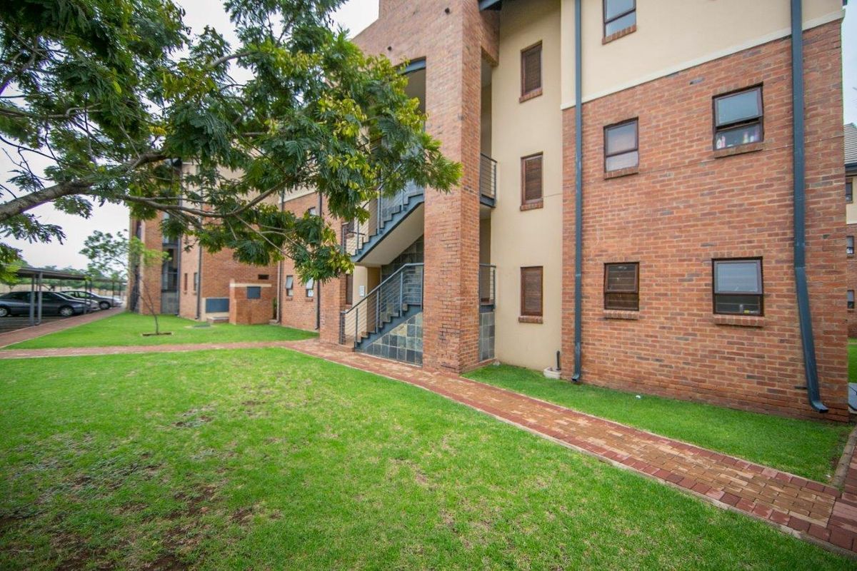 A view of the apartment complex exterior featuring face brick construction, an external staircase, and a well-maintained lawn with a paved walkway.