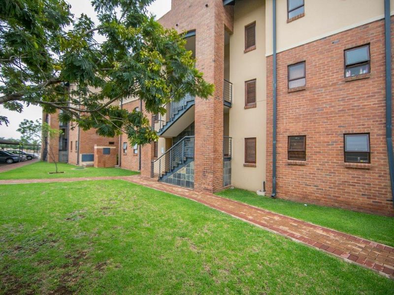 A view of the apartment complex exterior featuring face brick construction, an external staircase, and a well-maintained lawn with a paved walkway.