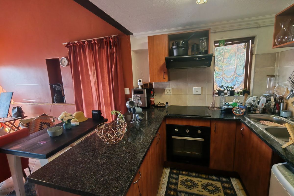 A functional kitchen featuring dark granite countertops, wooden cabinetry, a built-in oven, and an electric hob, adjacent to a dining area.