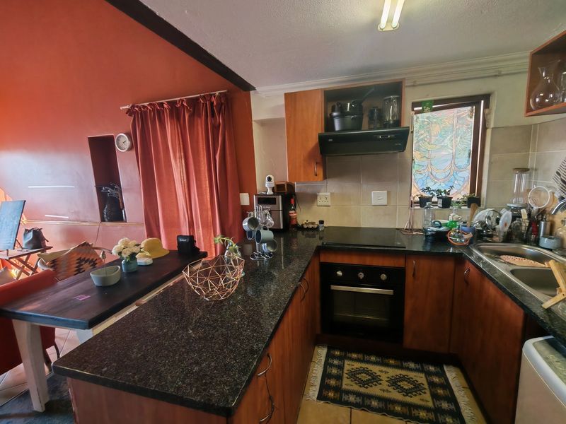 A functional kitchen featuring dark granite countertops, wooden cabinetry, a built-in oven, and an electric hob, adjacent to a dining area.
