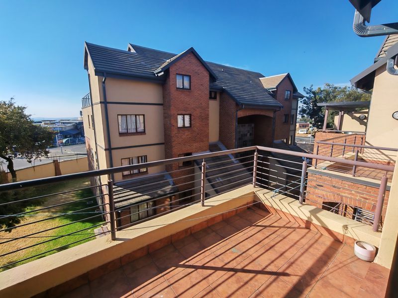 A spacious balcony with tiled flooring and metal balustrades, offering an elevated view of the apartment complex exterior and surrounding area.