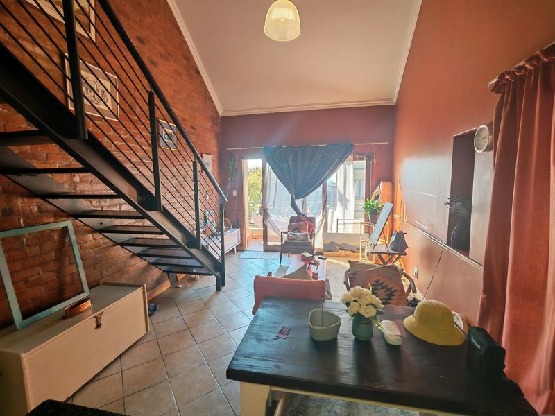 Spacious living area featuring an exposed brick wall, vaulted ceiling, and a metal staircase leading to an upper level, with access to a balcony.