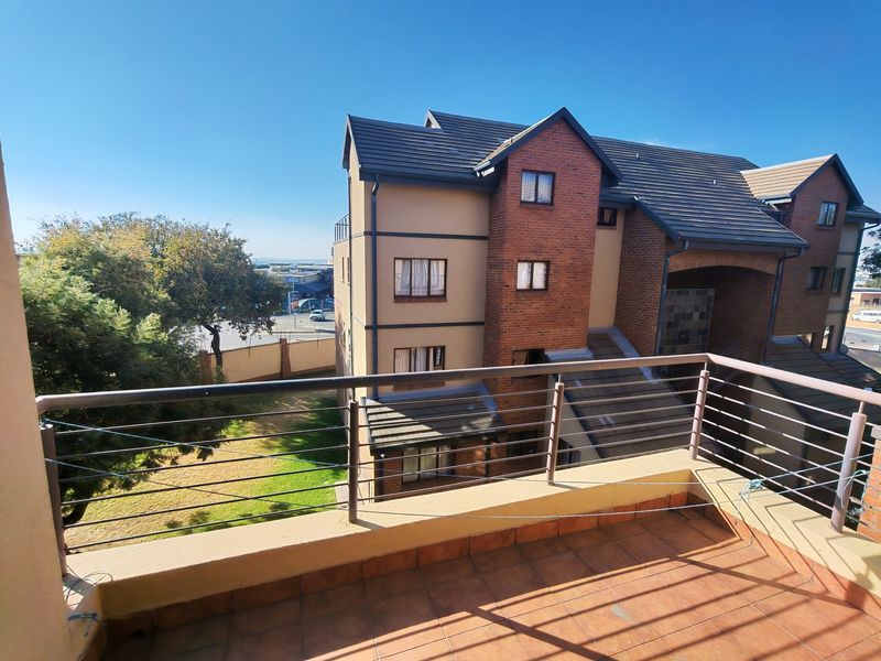 A spacious balcony with tiled flooring and a metal balustrade, offering an elevated view of the apartment complex and surrounding grounds.