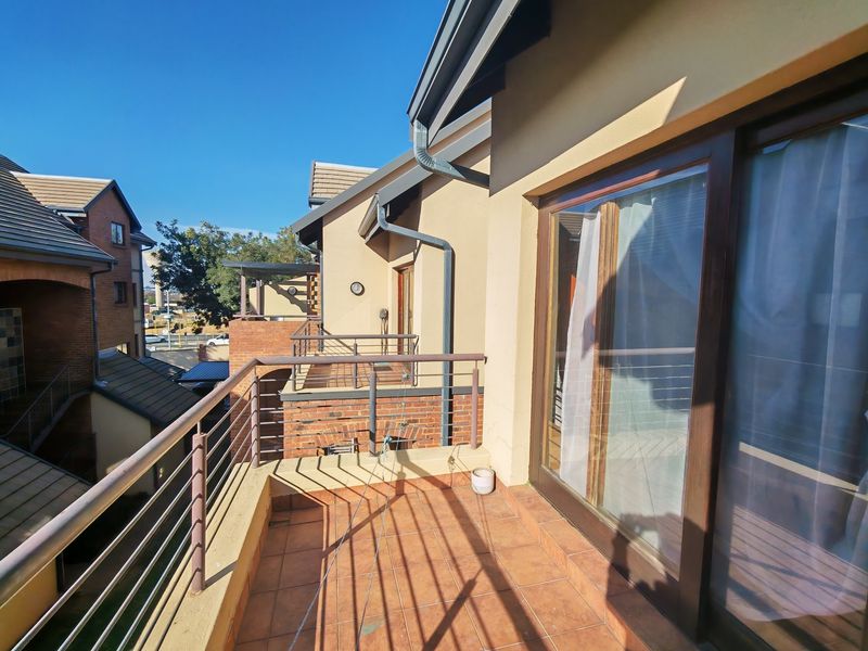 A spacious balcony featuring tiled flooring and a metal balustrade, accessible via large sliding glass doors, offering an elevated view of the surrounding complex.