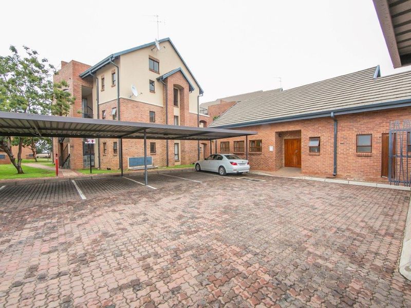 Exterior view of the apartment complex featuring a paved parking area with covered carports and face brick building facades.