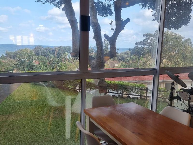 Enclosed balcony area featuring large glass windows with expansive views of the garden and ocean beyond.