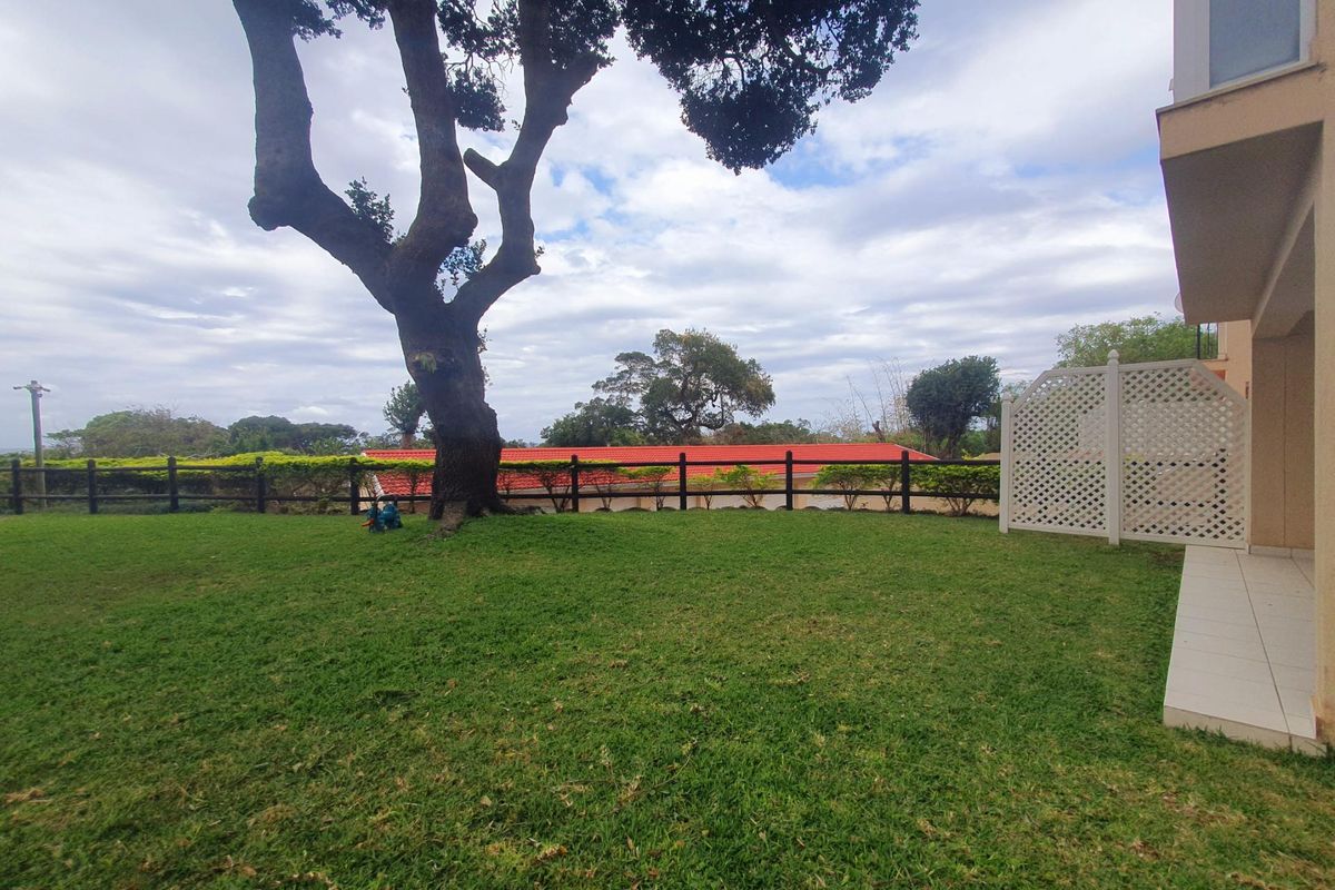 A private rear garden featuring a well-maintained lawn, mature tree, timber fencing, and a tiled patio area adjacent to the building.