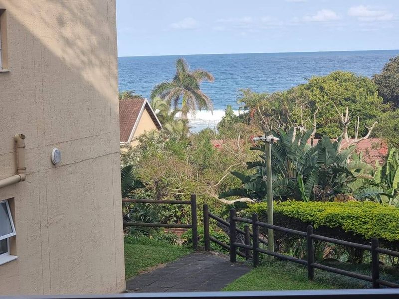 A view from the apartment looking out over the garden, surrounding greenery, and the ocean in the distance.