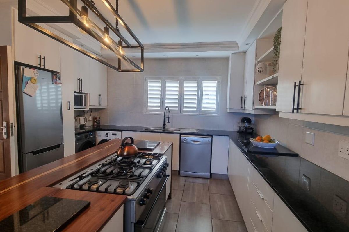 Modern kitchen featuring white cabinetry, granite countertops, a wooden island with a gas stove, and tiled flooring with shutter blinds.