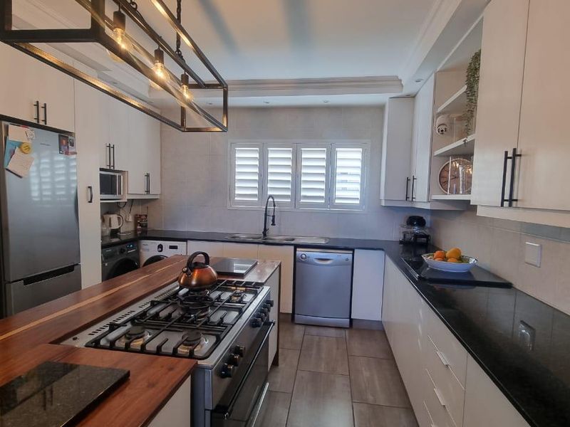 Modern kitchen featuring white cabinetry, granite countertops, a wooden island with a gas stove, and tiled flooring with shutter blinds.