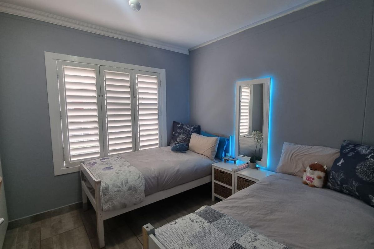 A well-maintained bedroom featuring tiled flooring, built-in wardrobe storage, and white plantation shutters providing natural light control.