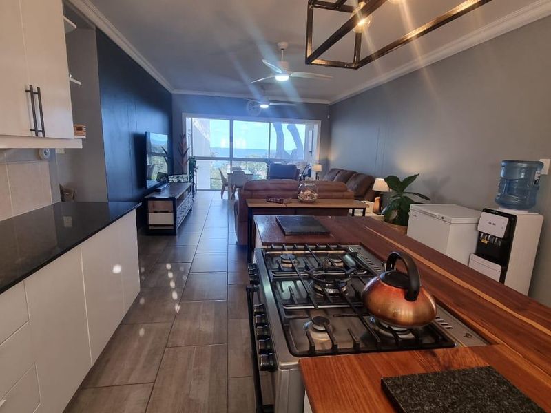 Spacious open-plan kitchen and living area featuring modern cabinetry, gas hob, tiled flooring, and large sliding doors leading to an outdoor balcony.