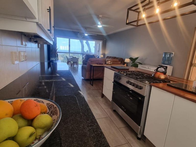 Open-plan kitchen and living area featuring granite countertops, a gas stove, tiled flooring, and direct access to a balcony through sliding glass doors.