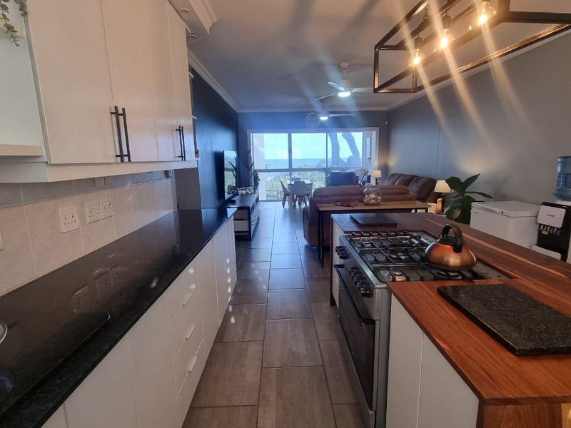 Open-plan kitchen and living area featuring modern white cabinetry, stone countertops, gas stove, and tiled flooring with direct access to a balcony.