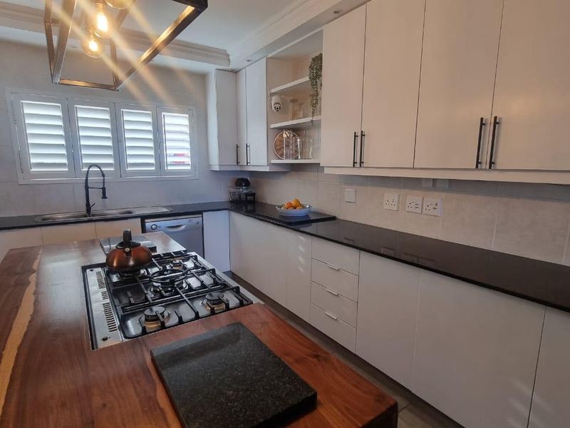 Modern kitchen featuring white cabinetry, dark stone countertops, a large wooden island with a gas hob, and integrated laundry appliances.