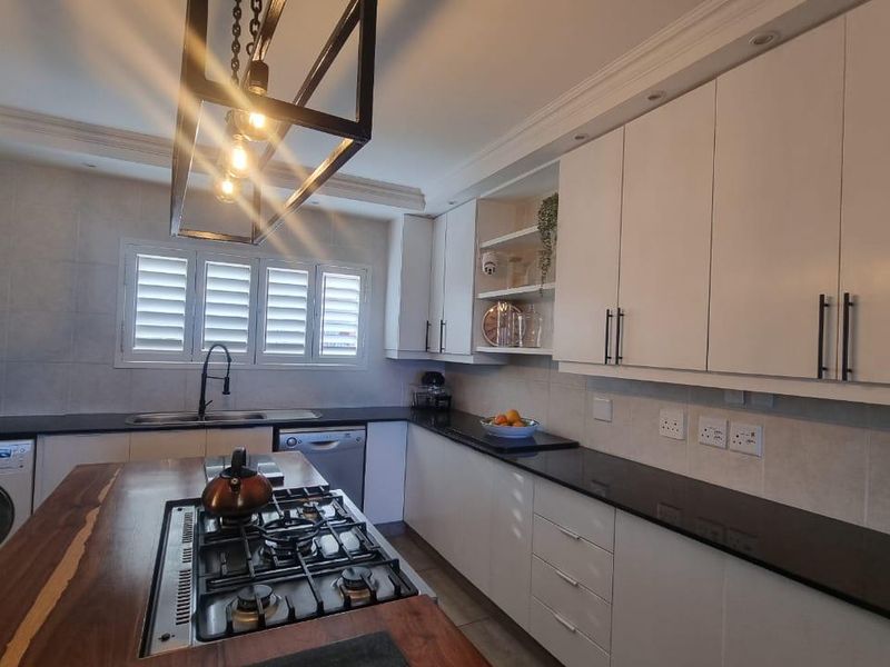 Modern kitchen featuring white cabinetry, dark granite countertops, a central island with a gas hob, and stylish pendant lighting.