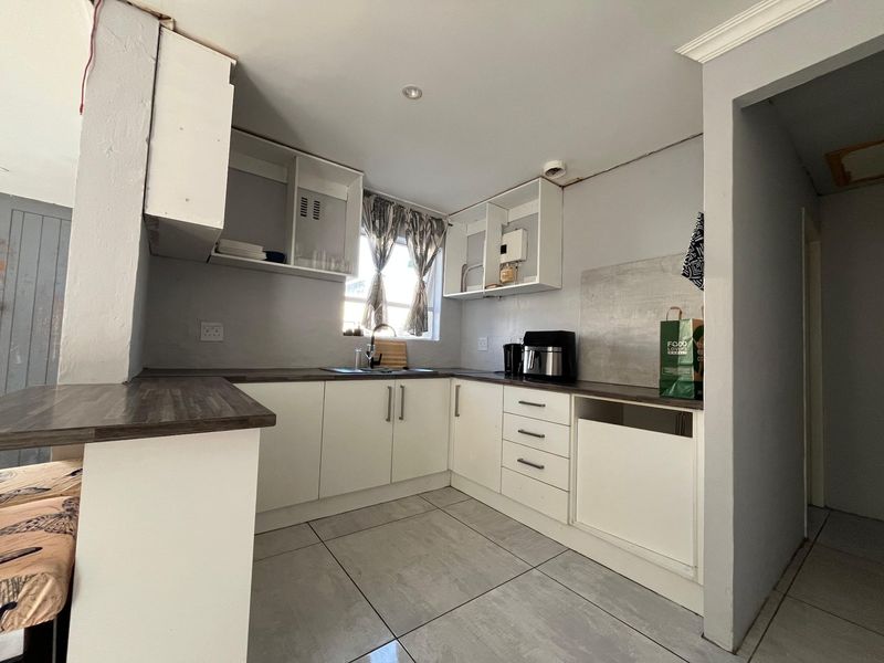 A compact kitchen featuring white cabinetry, laminate countertops, and tiled flooring, currently requiring some finishing touches to the cabinetry and wall edges.
