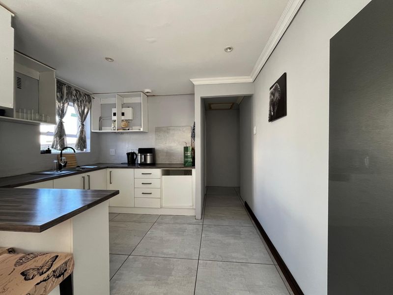 A functional kitchen featuring laminate countertops, built-in cabinetry, and tiled flooring, with an adjacent hallway leading to other areas of the home.