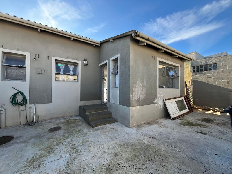 Rear exterior view of the property featuring a concrete patio area, external wall lighting, and casement windows with weathered exterior finishes.