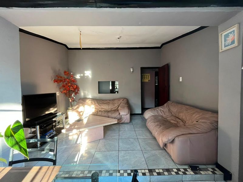 A living room featuring tiled flooring and dark coving, currently showing signs of wear including ceiling damage and dated wall finishes.