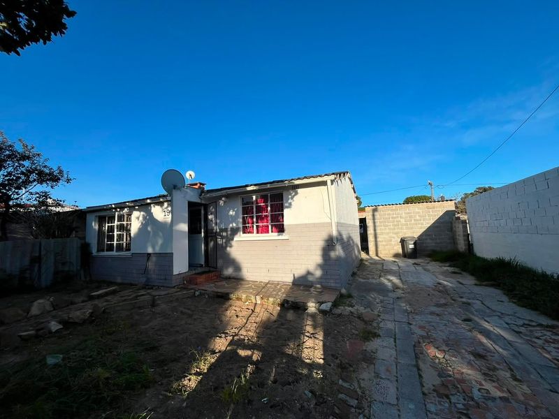 Front exterior view of a single-story house featuring a paved driveway, security gate, and satellite dish, set on a residential plot.