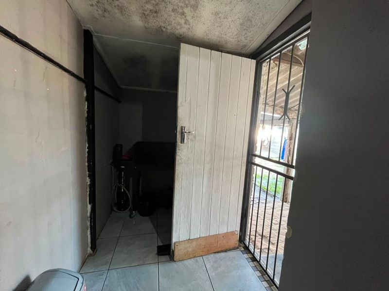 A small utility space featuring tiled flooring, a timber door, and a security gate, currently showing signs of significant wear and ceiling damage.