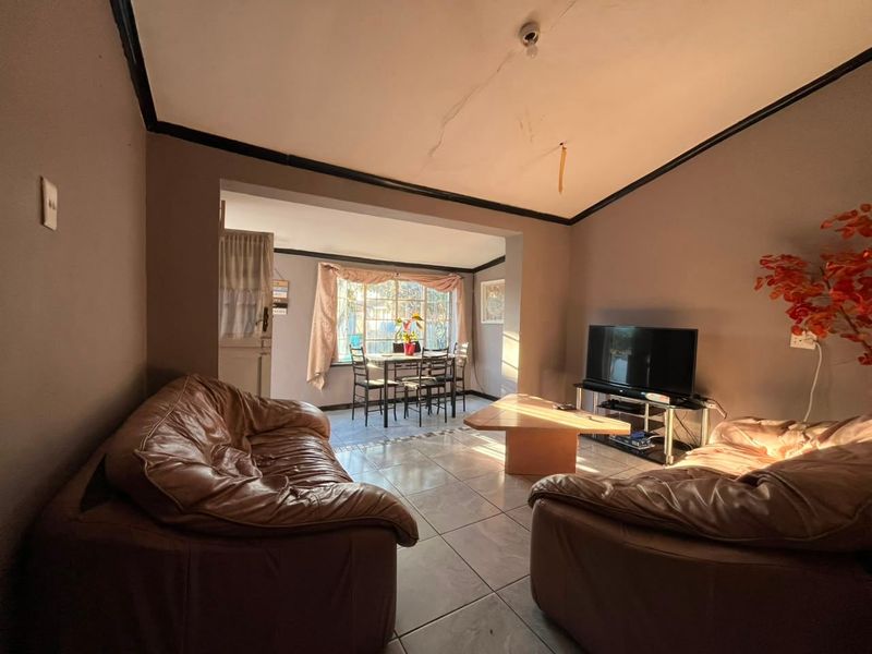 Open plan living and dining area featuring tiled flooring and large windows, requiring ceiling repairs and general cosmetic updates.