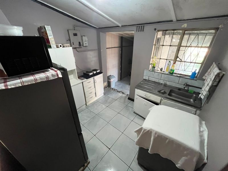 A compact kitchen featuring tiled flooring, built-in cabinetry, and a stainless steel sink, requiring cosmetic updates to improve its overall condition and functionality.