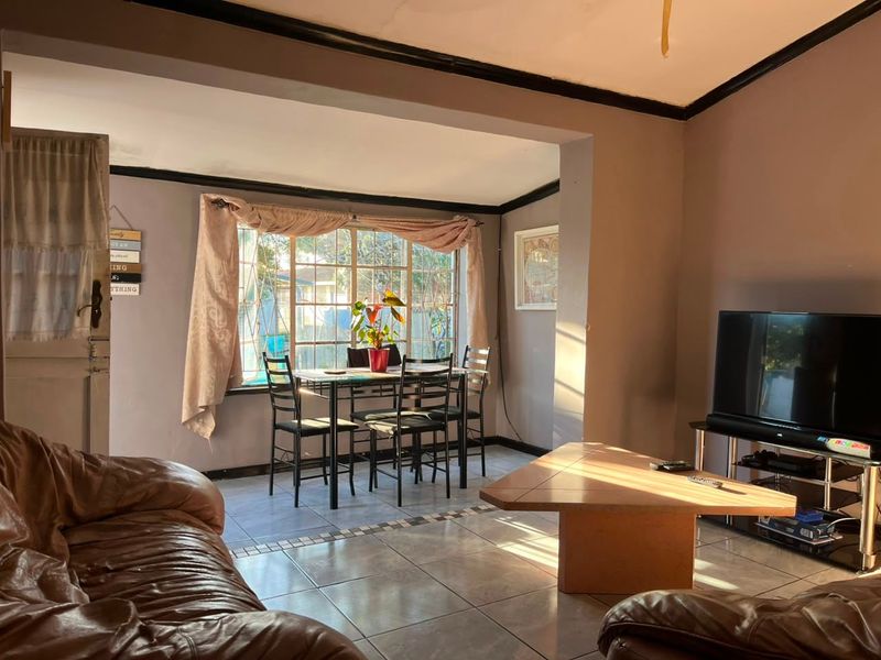 An open-plan living and dining area featuring tiled flooring, large windows with security bars, and neutral wall finishes.