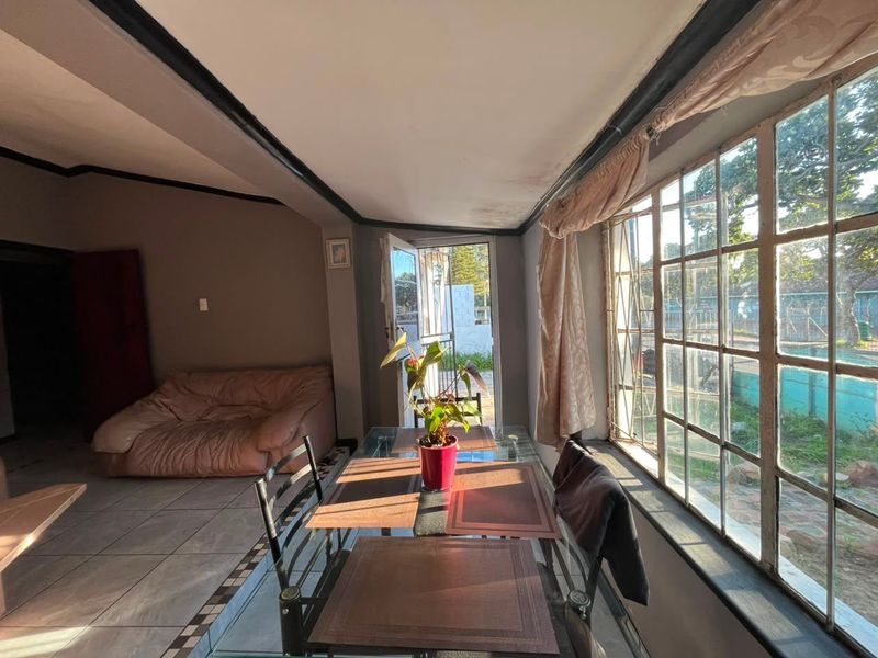 A living area featuring tiled floors and large steel-framed windows, with visible signs of ceiling water damage requiring maintenance.