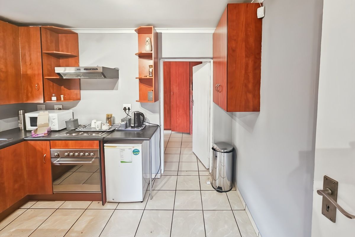 A functional kitchen featuring wood-finish cabinetry, built-in oven with extractor fan, and tiled flooring, leading into an adjacent hallway.