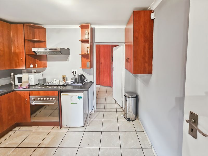 A functional kitchen featuring wood-finish cabinetry, built-in oven with extractor fan, and tiled flooring, leading into an adjacent hallway.