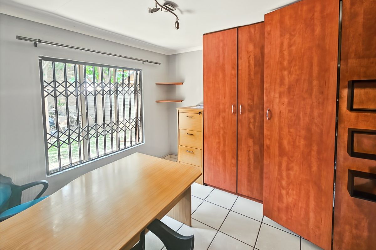 A bedroom featuring built-in wooden cupboards, tiled flooring, and a window fitted with a security gate.