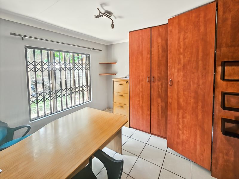 A bedroom featuring built-in wooden cupboards, tiled flooring, and a window fitted with a security gate.